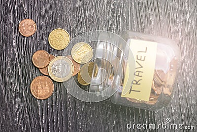 Tilted glass jar with scattered euro coins with the inscription TRAVEL on a black wooden table Stock Photo