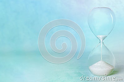 Time. An hourglass with flowing sand on a pastel blue background Stock Photo
