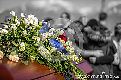 Funeral Casket In Color and Focus, With Family Mourning in Background Out of Focus and In Black And White Stock Photo