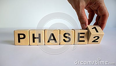 Time for Phase 2. Hand is turning a cube and changes the word `Phase 1` to `Phase 2`. Beautiful white background. Business con Stock Photo