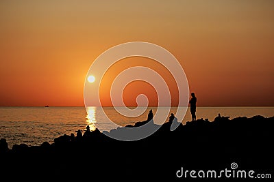 Time of sunset on the Black Sea. Silhouettes of pyramids of stones on the shore and men. Orange color. Stock Photo