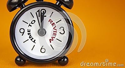 Time to review symbol. Beautiful black alarm clock with words `time to review`. Beautiful orange background. Copy space. Busines Stock Photo