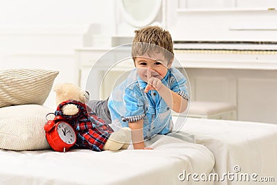 Time to sleep concept. Child in bedroom with silence gesture. Boy with happy face puts favourite toy on bed, time to Stock Photo