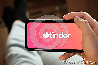 Tinder logo on the smartphone screen in mans hand. Man using tinder application for dating and looking for love, July Editorial Stock Photo