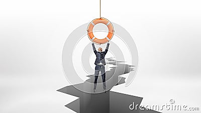 A tiny businessman holds on to a red life buoy hanging above a large earthquake rift. Stock Photo