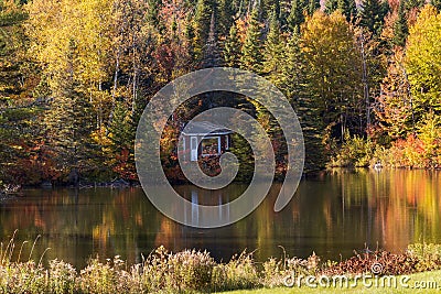 Tiny cabin nestled in colourful fall foliage at the edge of a small lake Stock Photo