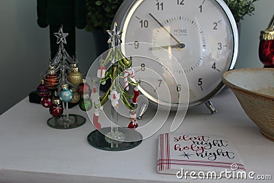 Tiny Christmas decorations including glass miniature trees and ornaments and a coaster sitting on a coffee table with a clock Stock Photo