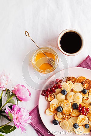 Tiny pancakes with berries, honey, flowers, coffee. Pancake cereal. The concept of Breakfast, food trends. Copy space Stock Photo