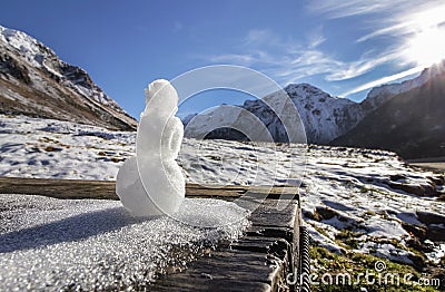 A tiny snowman stands against the backdrop of snow-capped mountains on a sunny day. Beautiful autumn valley in the background Stock Photo