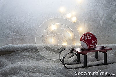 Tiny toy sledges with Christmas ball on window sill covered with white snow. Winter and Christmas outdoor decoration. Stock Photo