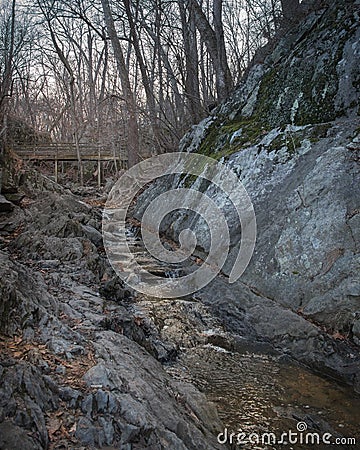 Tiny waterfall below a simple bridge where one can take simple breaks. Stock Photo