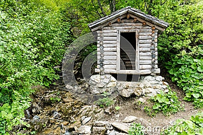 Tiny wooden mountain cabin in dense lush green summer forest with a small creek beside it Stock Photo