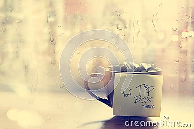 Tip box, coin in the coffee cup in cafe front of mirror and rain water drop, Vintage color and soft Stock Photo