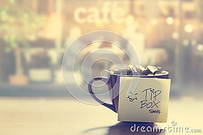 Tip box, coin in the coffee cup in cafe front of mirror, Vintage color and soft Stock Photo