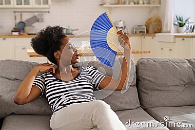 Black woman suffering from heatstroke flat without air-conditioner waving fan lying on couch at home Stock Photo