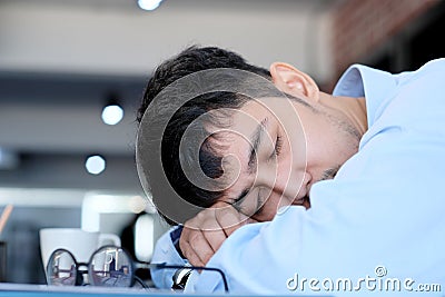 Tired asian man sleeping at office desk. Young businessman with eyeglasses overworked and fell asleep, Creative casual man Stock Photo