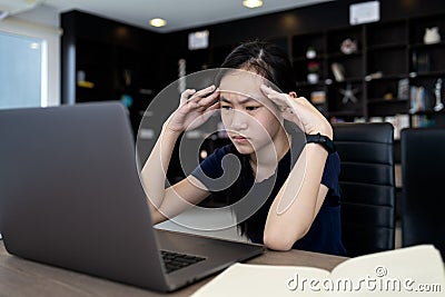 Tired asian student working at desk,use laptop computer for a long time on job,touching head with her hands,girl having a headache Stock Photo