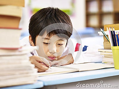 Tired and bored asian schoolboy doing homework in classroom Stock Photo