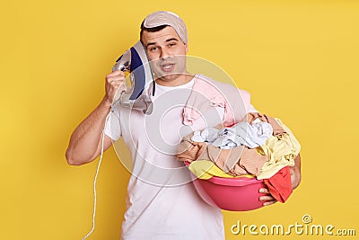 Tired bored young houseman househusband with iron near ear, being very tired, imagines he talking phone, need ironing clothes, Stock Photo