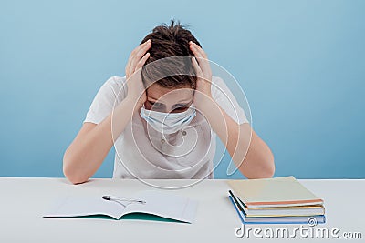 Tired boy with medical mask your hands on your head, sitting at the table Stock Photo