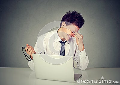 Tired business man rubbing eye sitting at table with laptop Stock Photo