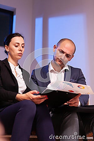 Tired businessman reading deadline raport with businesswoman doing overtime. Stock Photo