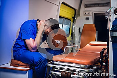 Tired corpsman in uniform sits inside the ambulance car and puts his hands on head Stock Photo