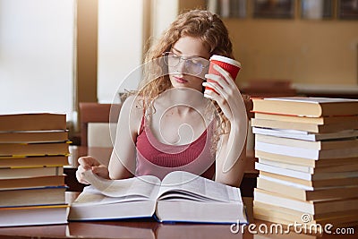 Tired determined college student searching for appropriate information for her project, reading texts, putting papercup of drink Stock Photo