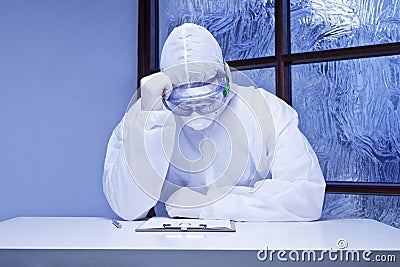 Tired doctor with protective clothing because of coronavirus in his medical practice Stock Photo