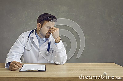 Tired exhausted male doctor sitting at the table after a hard day's work. Medical everyday life. Stock Photo