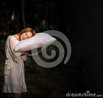 A tired, exhausted woman sleeps on a pillow she holds in her hands in the woods. Desire to sleep, time but rest concept. Place for Stock Photo