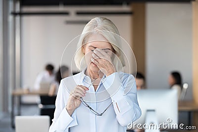 Tired fatigued senior female employee taking off glasses feeling eyestrain Stock Photo