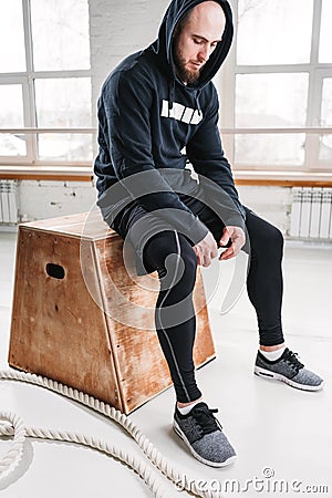 Tired fit man wearing black hoodie sitting on box at light hall Stock Photo