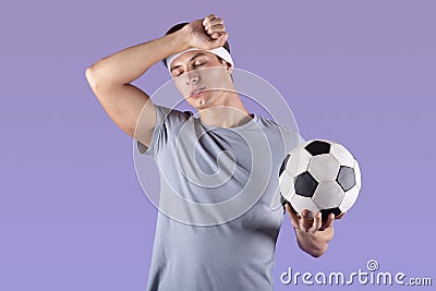 Tired football player with ball wiping sweat after game or championship over lilac studio background Stock Photo