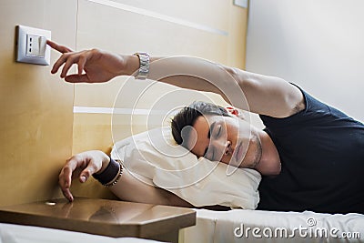 Tired Guy Switching off Light While Lying on Bed Stock Photo