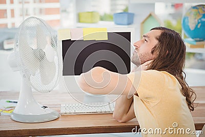 Tired hipster sitting by electric fan on desk Stock Photo