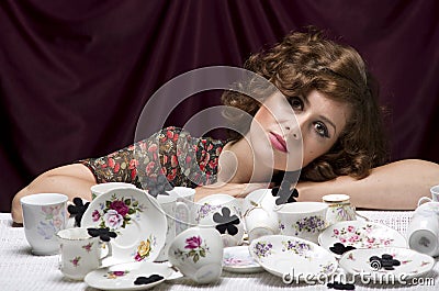 Tired housewife. A pretty woman sitting at a table with lots of cups saucers coffee service. Stock Photo