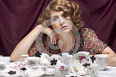 Tired housewife. A pretty woman sitting at a table with lots of cups saucers coffee service. Stock Photo