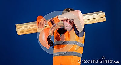 Tired labourer concept. Man in helmet and protective gloves wiping sweat from forehead, blue background. Carpenter Stock Photo