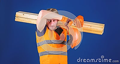 Tired labourer concept. Man in helmet and protective gloves wiping sweat from forehead, blue background. Carpenter Stock Photo