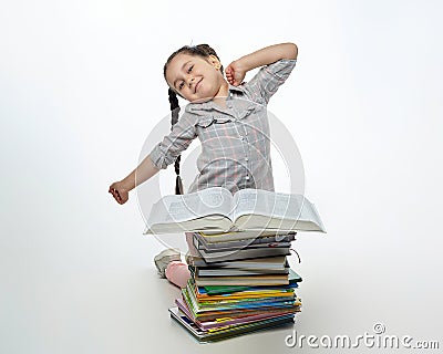 Tired little girl sits in front of a large stack of books and stretches Stock Photo