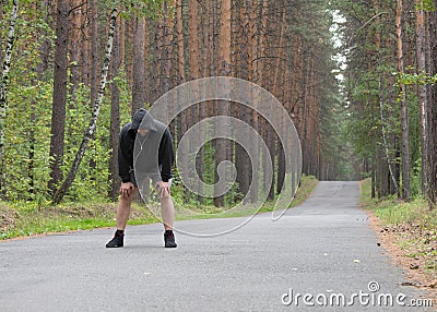 Tired man in grey hoodie making a stop after jogging on road in the forest, selective focus Stock Photo