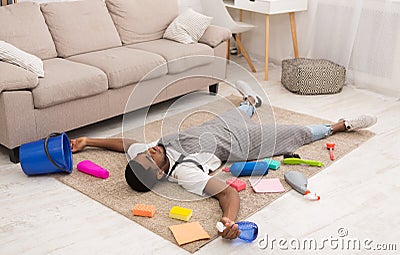 Tired man lying on carpet surrounded by cleaning supplies Stock Photo