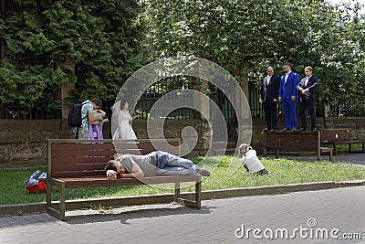 Tired Man sleeping on a bench while photographer taking pictures for wedding procession Editorial Stock Photo