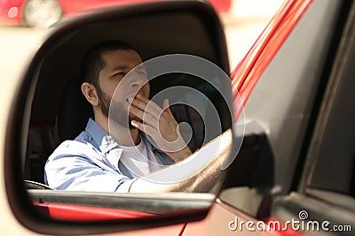 Tired man yawning in auto, view through car side mirror Stock Photo