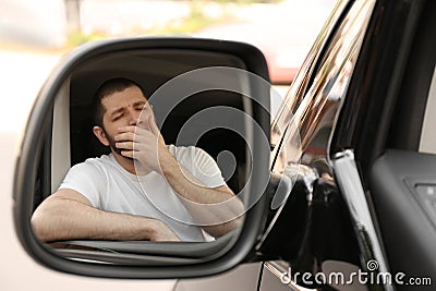 Tired man yawning in auto, view through car side mirror Stock Photo