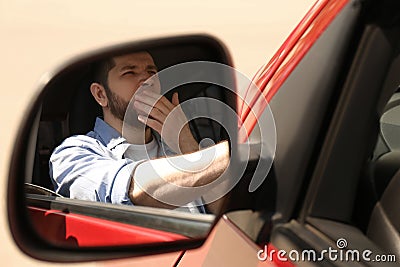 Tired man yawning in auto, view through car side mirror Stock Photo