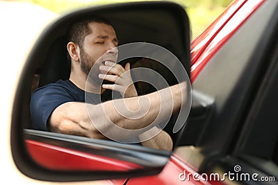 Tired man yawning in auto, view through car side mirror Stock Photo