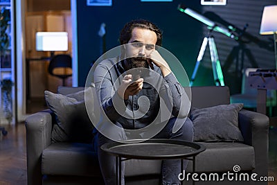 Tired man zapping through channels, watching news broadcast on TV Stock Photo