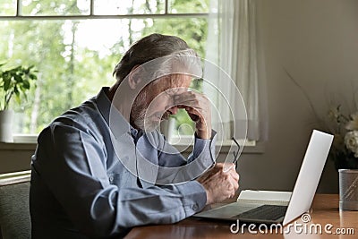 Tired mature 60s man working at laptop from home Stock Photo